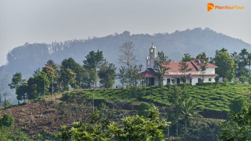 a white building with a red roof and a red roof on a hill with trees : Wayanad , Kerala