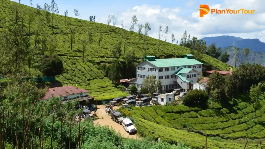 a building of Kolukkumalai Tea Estate with cars parked in front of a green hill
