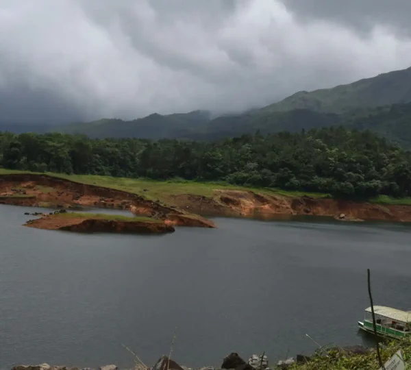 A serene lake with a small island rests within Wayanad's lush green hills under a cloudy sky Near Banasurasagar Dam.