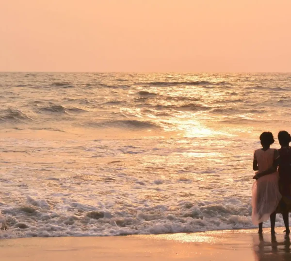 A couple stands on a Calicut beach, embracing as they watch the sunset over the ocean