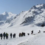 A group of people trekking up a snowy mountain, surrounded by a winter landscape and clear blue skies at Sar Pass Trek.