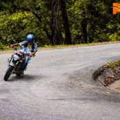 A motorcyclist navigates a winding road surrounded by lush greenery in Gap Road, Munnar.