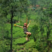 Smiling woman in a helmet glides on a Zipline in Wayanad above lush tea plantations and forested hills, enjoying an adventurous outdoor ride.