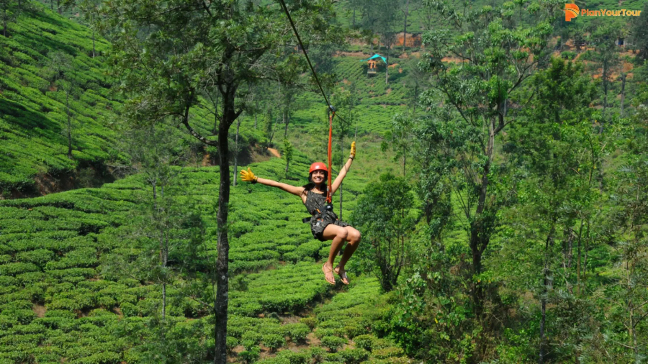 Smiling woman in a helmet glides on a Zipline in Wayanad above lush tea plantations and forested hills, enjoying an adventurous outdoor ride.